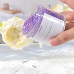 Load image into Gallery viewer, Hand pouring purple lavender bath salts from jar with white flower beside bathtub