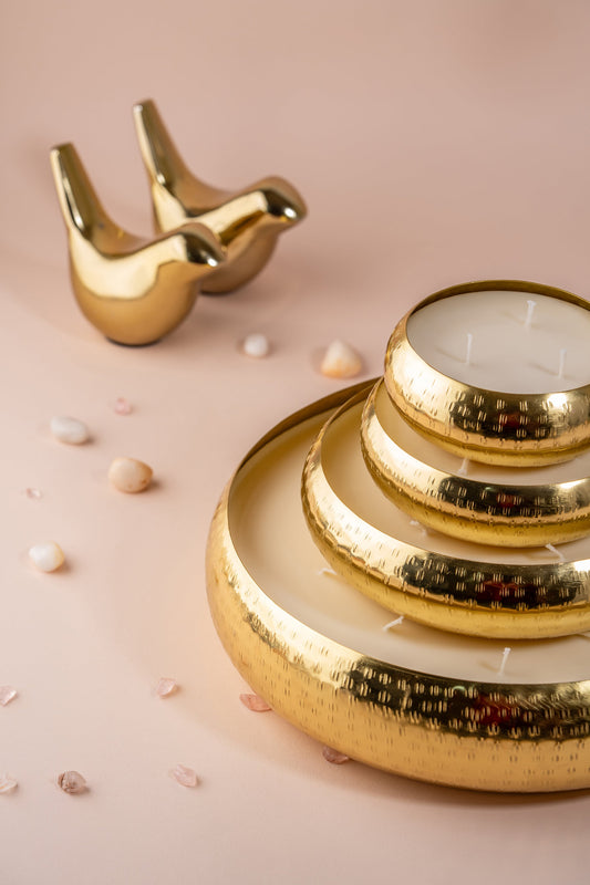 Gold hammered metal candle bowls and decorative bird figurines on beige background