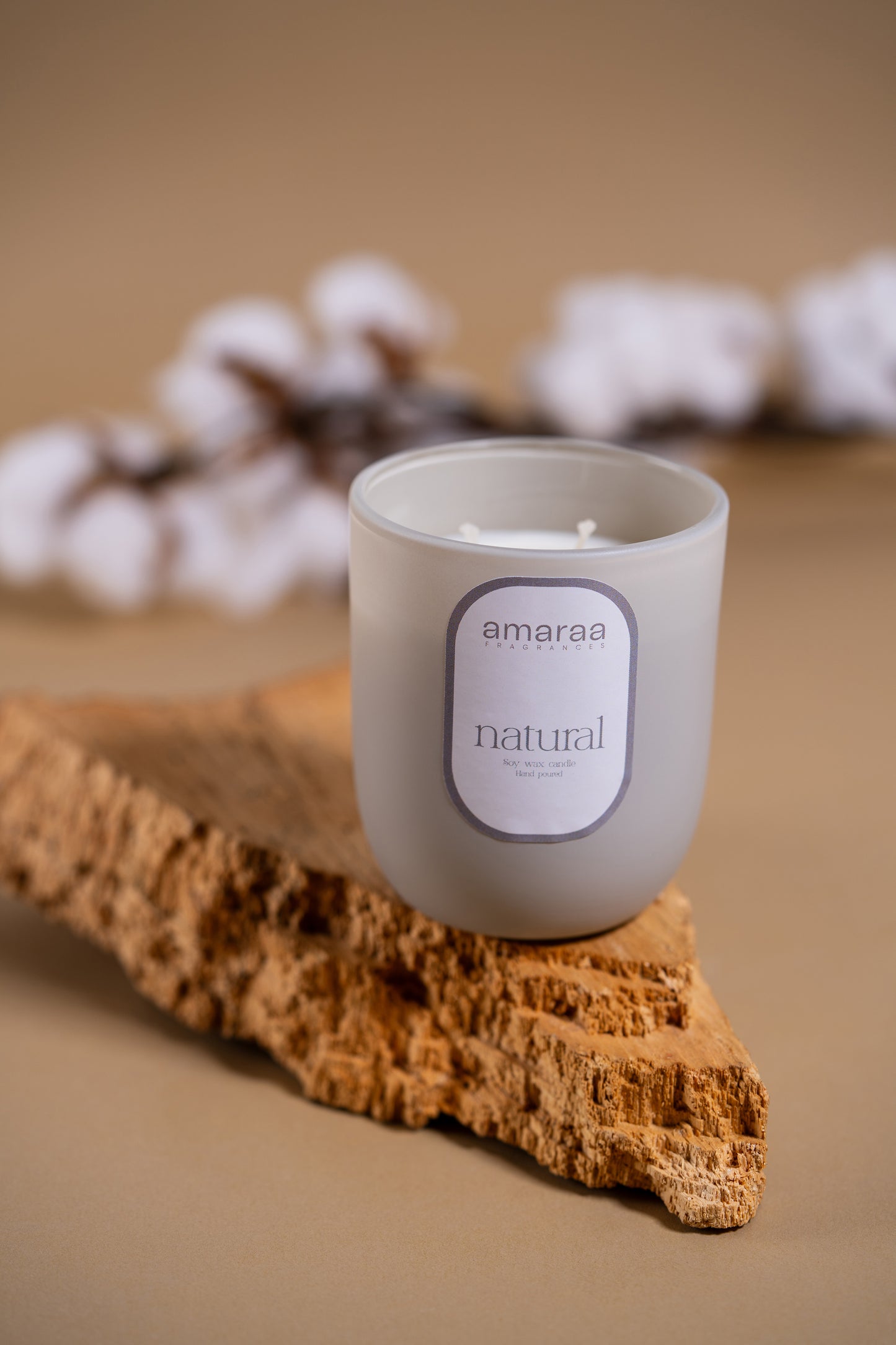 Amaraa natural soy wax candle in frosted glass on cork with cotton flowers, beige background