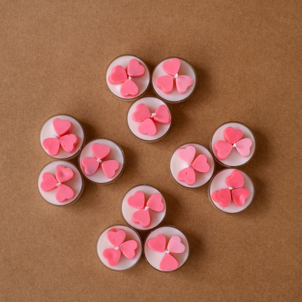 Pink heart-shaped tealight candles arranged on brown background
