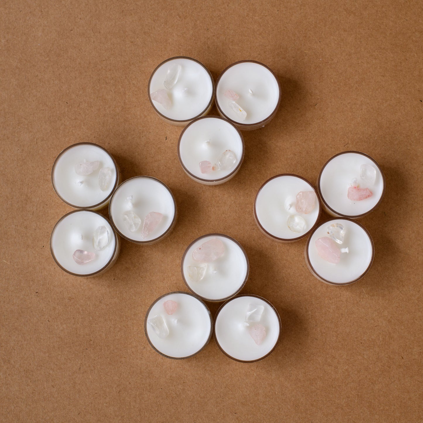white tealight candles with rose quartz and clear crystals on brown background