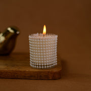 Decorative beaded glass candle burning on wooden tray with brown background