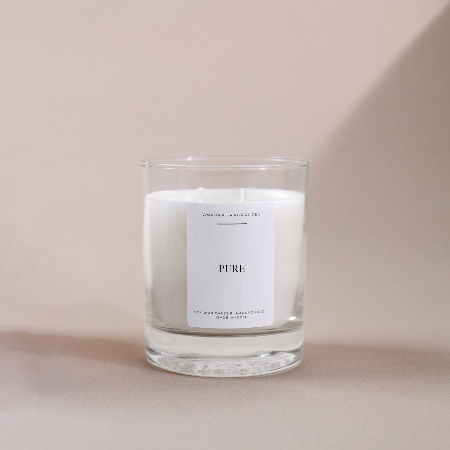 White soy wax candle in a clear glass jar with Pure label on a beige background