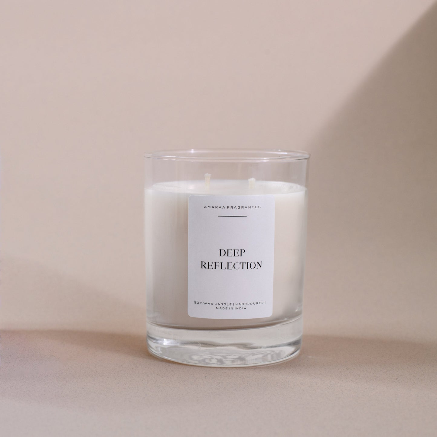 Clear glass soy wax candle labeled 'Deep Reflection' by AMARAA Fragrances on beige background.