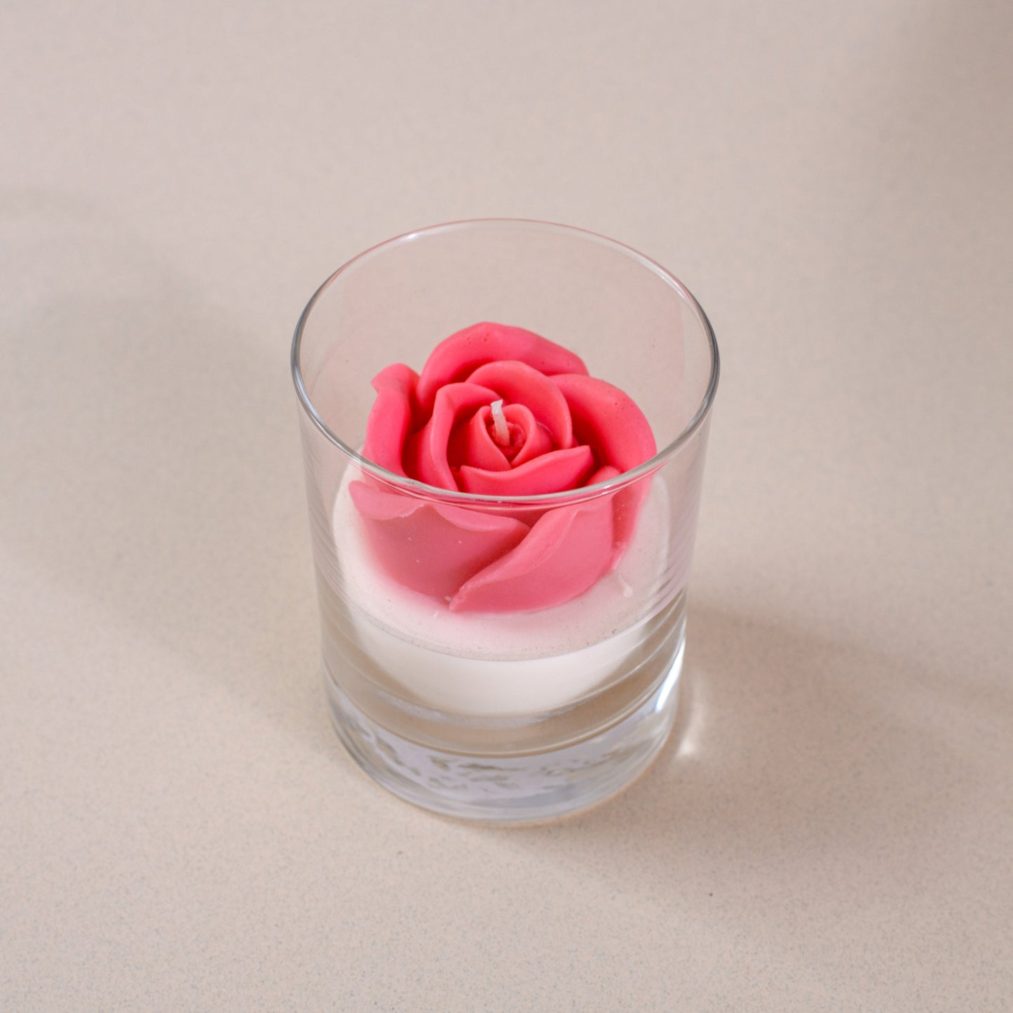Pink rose-shaped candle in a clear glass holder on a beige surface