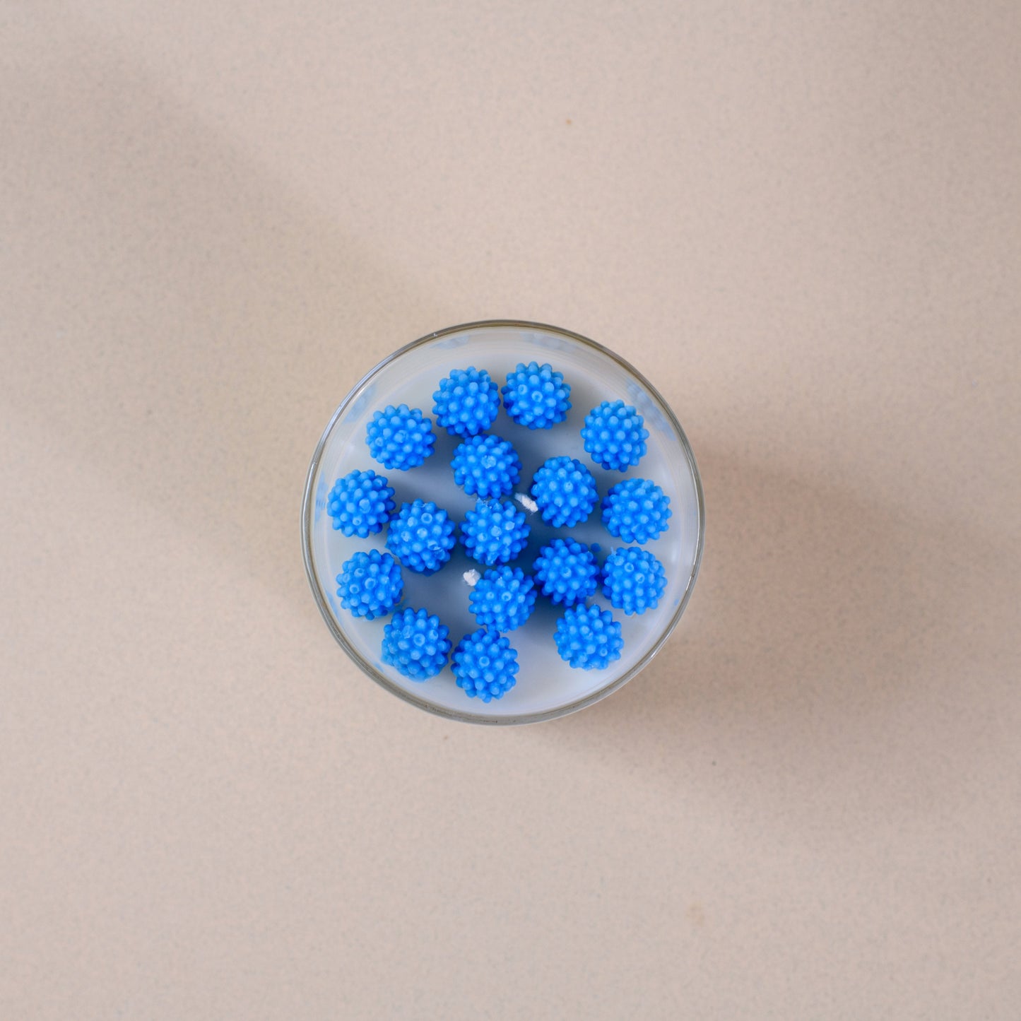 Glass of milk with spiky blue balls on a beige surface, minimalist top view