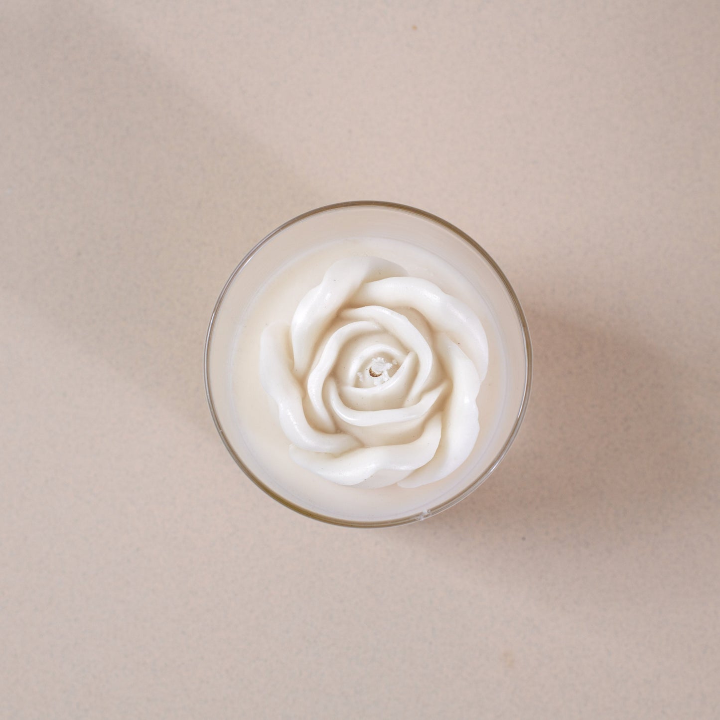 White rose-shaped candle in a glass on a light beige background