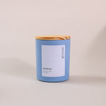 Load image into Gallery viewer, Blue soy wax candle with wooden lid and white label on neutral background