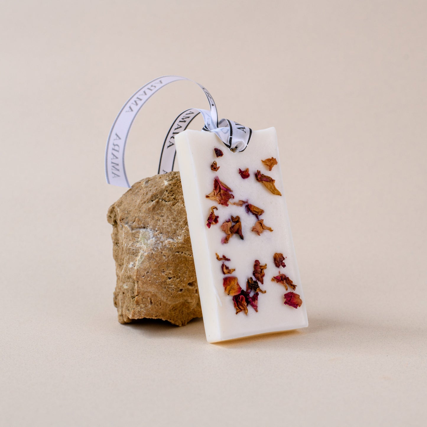 White wax sachet with dried rose petals and ribbon, displayed on a natural stone