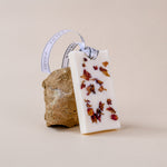Load image into Gallery viewer, White wax sachet with dried rose petals and ribbon, displayed on a natural stone