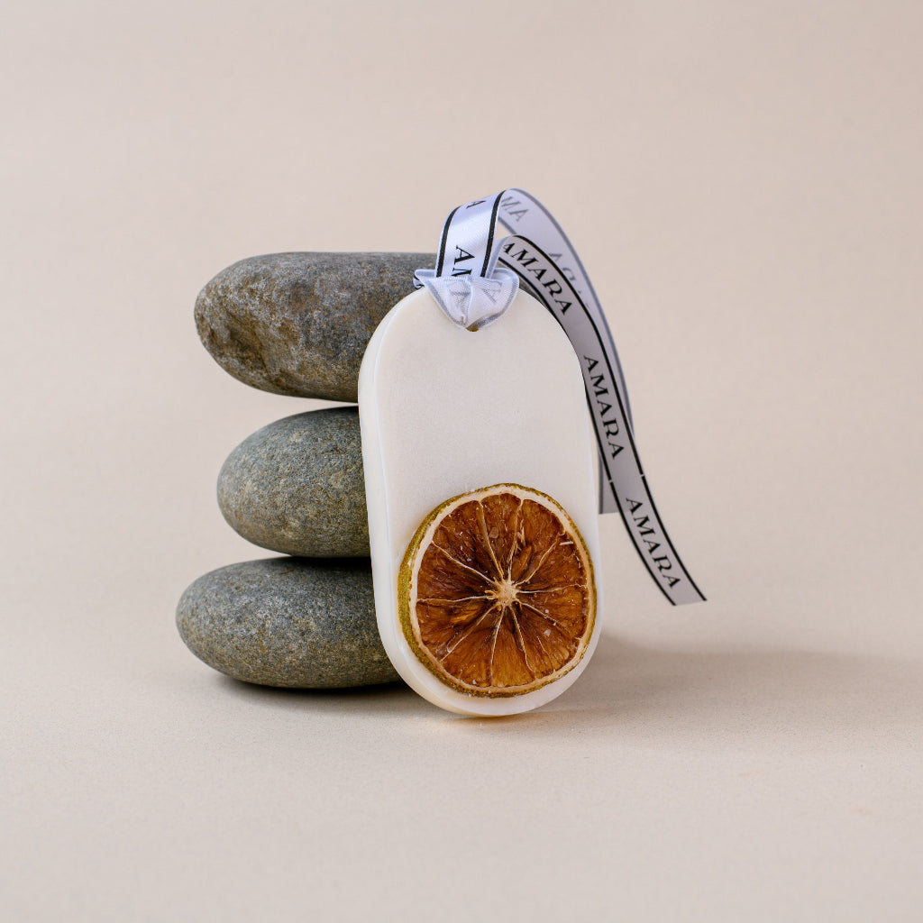 Scented wax tablet with dried orange slice and branded ribbon, stacked stones background