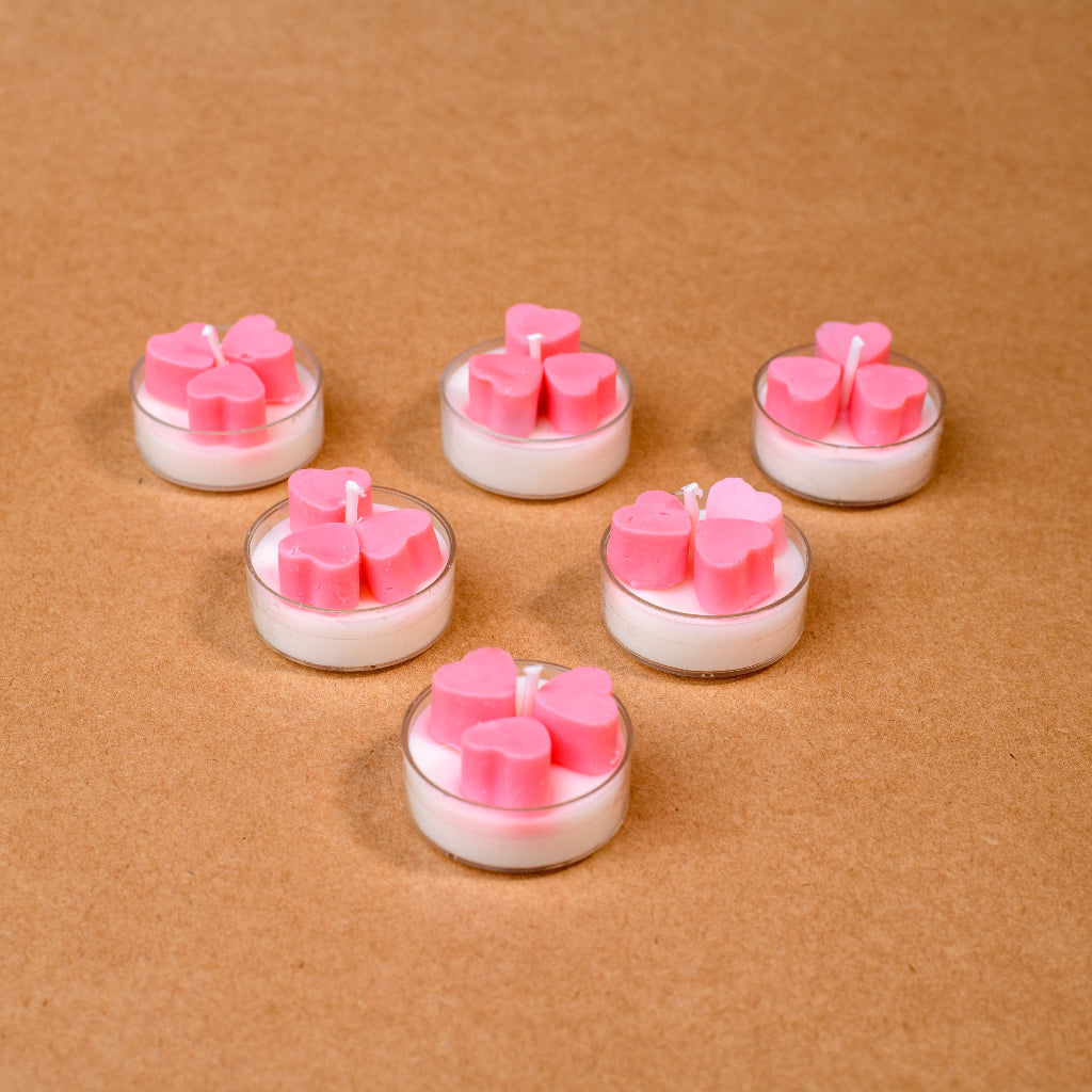 Six tealight candles with pink heart shapes on brown background