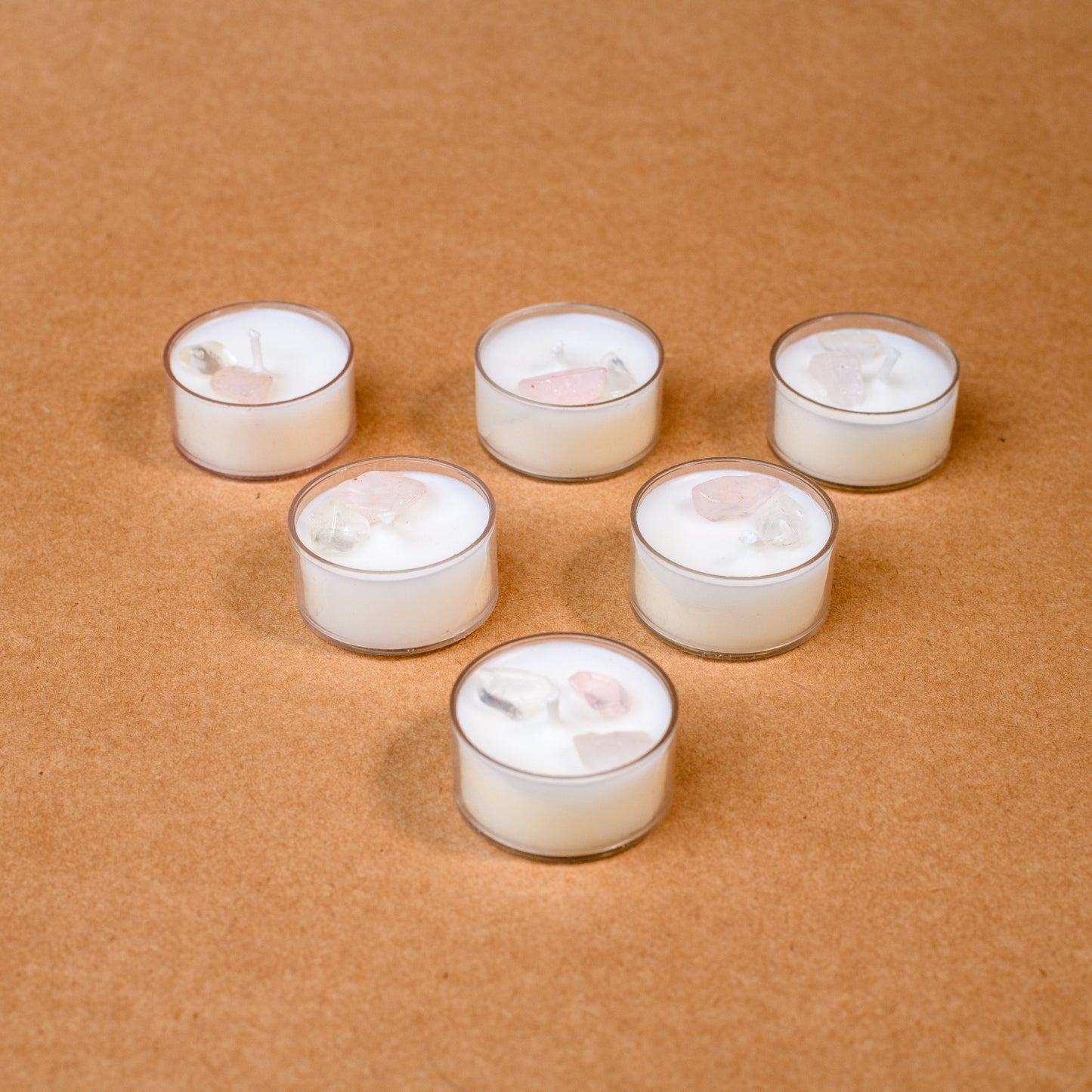 Six white tealight candles with crystals on brown background