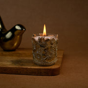 Decorative floral glass candle burning on wooden tray with gold bird figurine
