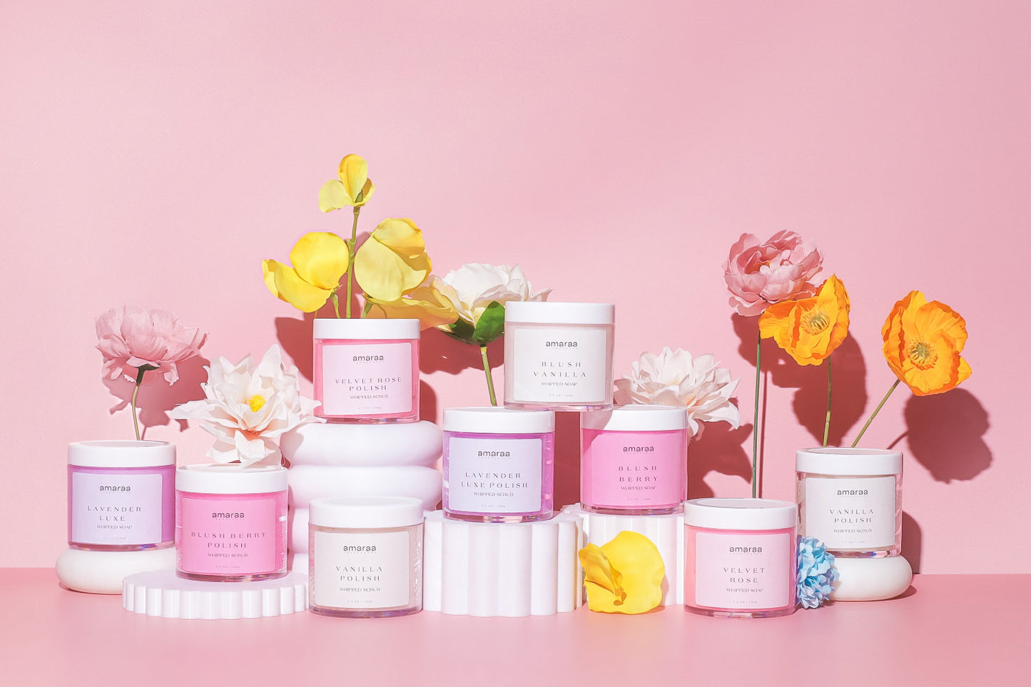 Amaraa whipped scrubs in colorful jars with spring flowers on a pink background