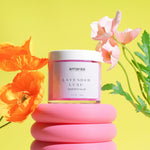 Load image into Gallery viewer, Amaraa Lavender Luxe whipped soap jar with colorful flowers on a pink stand, yellow background
