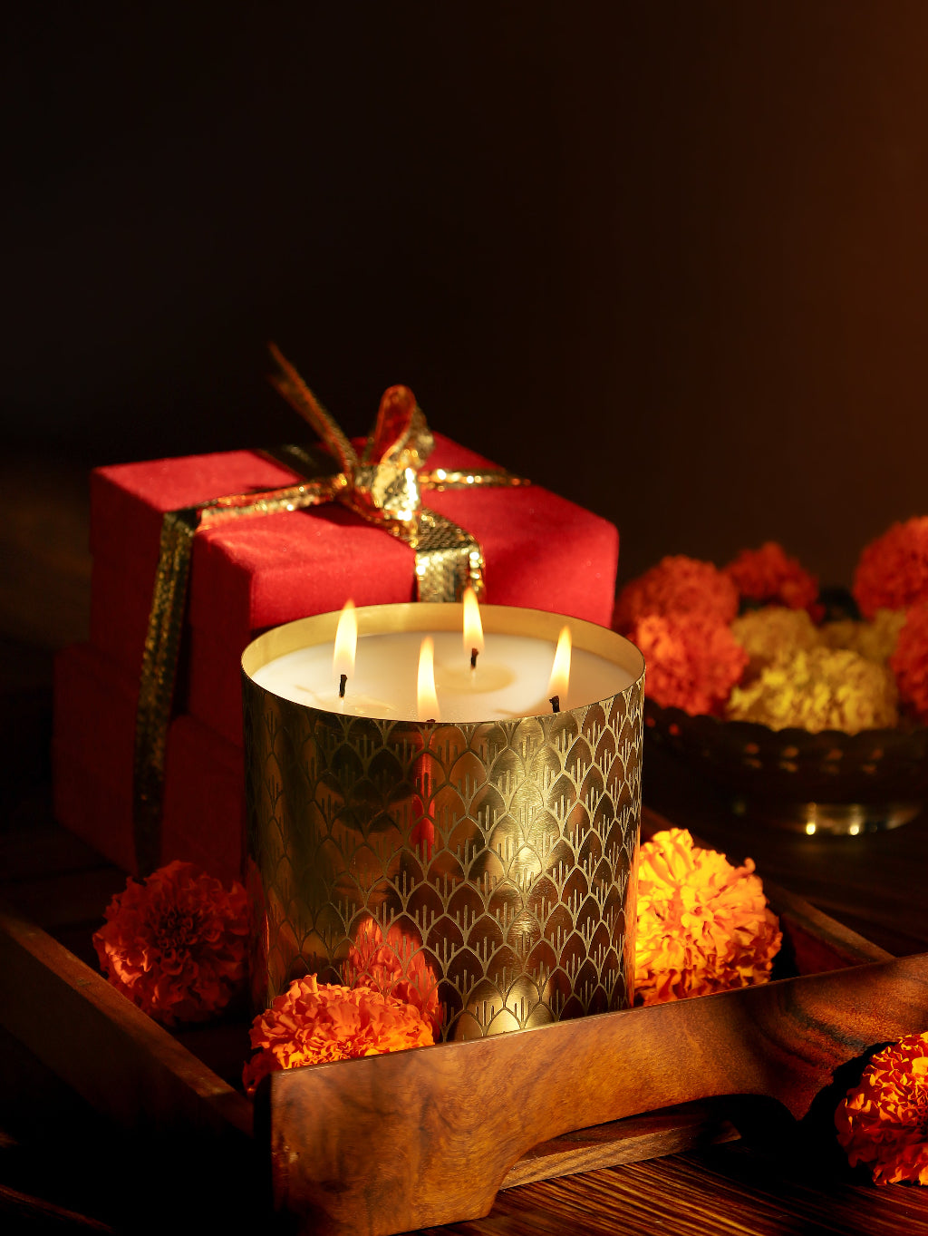 Decorative gold candle with marigold flowers and red gift box on wooden tray