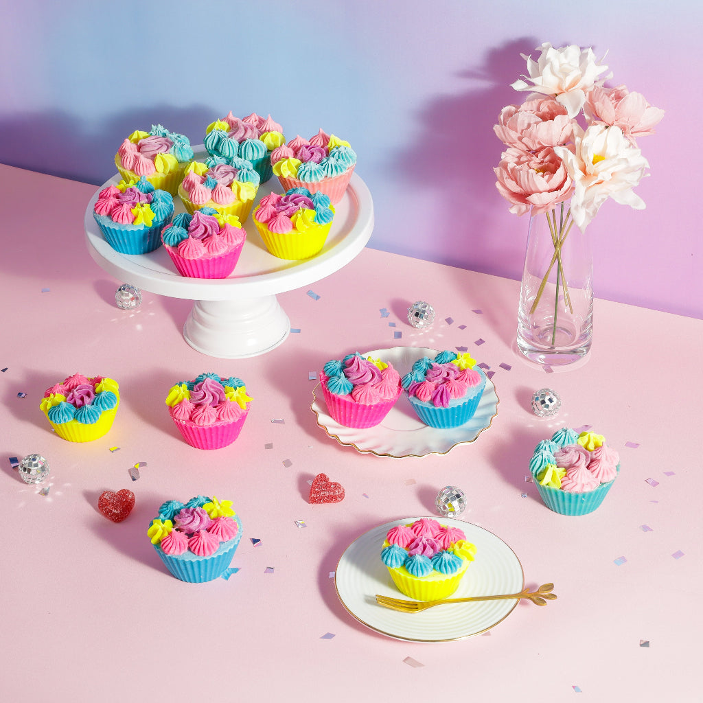 Colorful cupcakes with pink, blue, and yellow frosting on pastel table with flowers and confetti