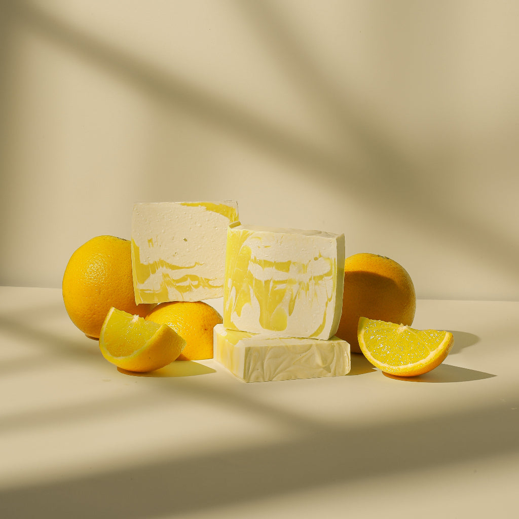 Lemon soap bars with fresh lemons and lemon slices on a neutral background