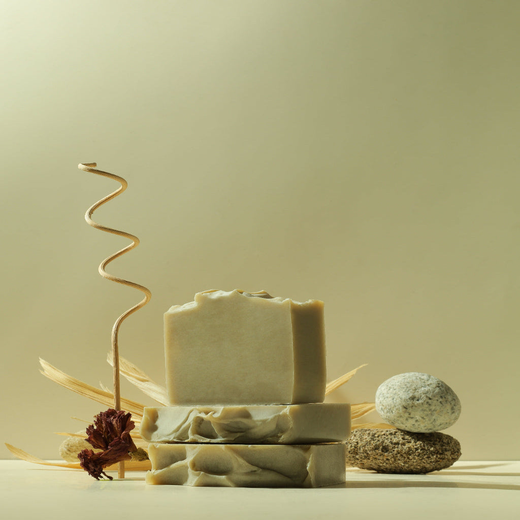 Handcrafted natural soap bars stacked with stones and dried flower on a neutral background