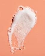 Load image into Gallery viewer, White soap foam with bubbles on a peach background, skincare product texture