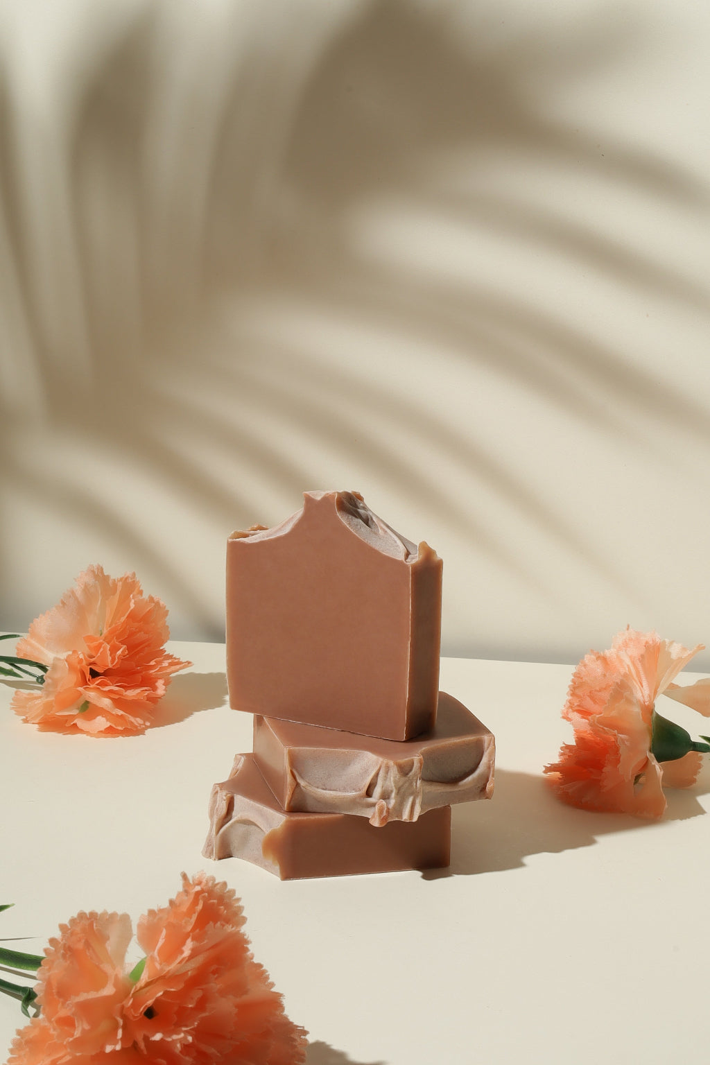 Natural handmade soap bars with peach flowers on a cream background, beauty product flat lay