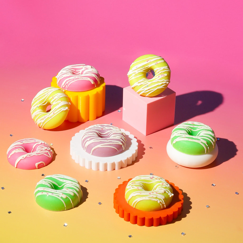 Colorful donuts with icing displayed on pastel geometric stands against a pink gradient background