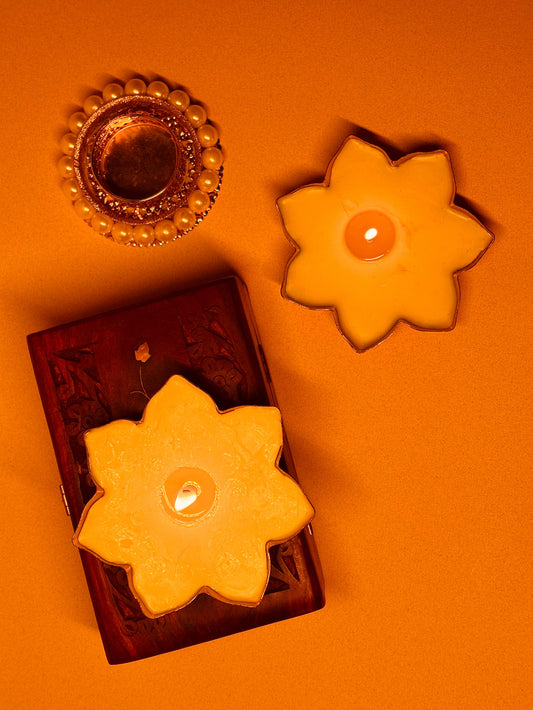 Yellow flower-shaped candles and decorative diya on orange background, festive decor