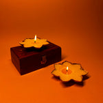 Load image into Gallery viewer, Two yellow flower-shaped candles, one on a wooden box, on an orange background