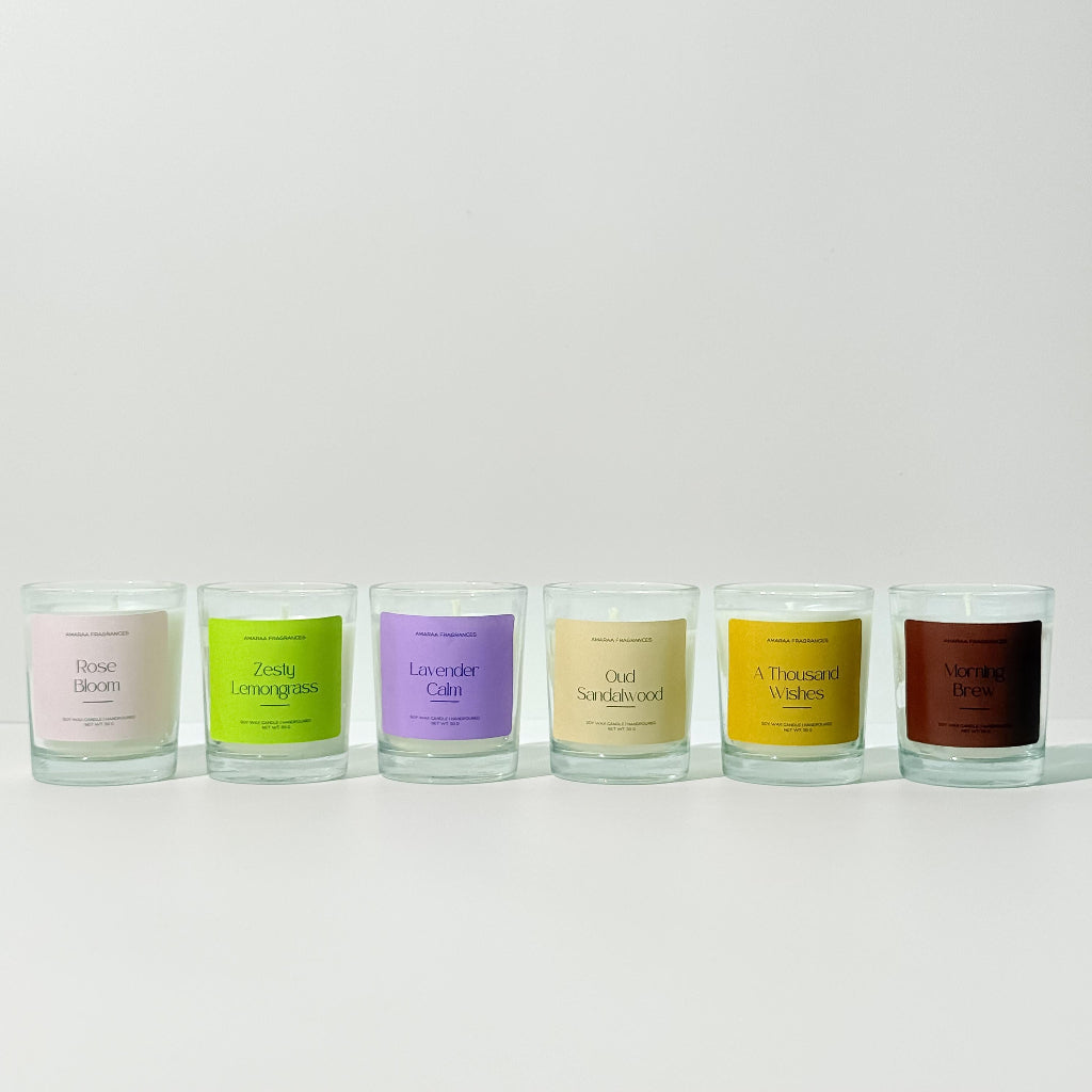 Six scented candles in glass jars with colorful labels on a white background