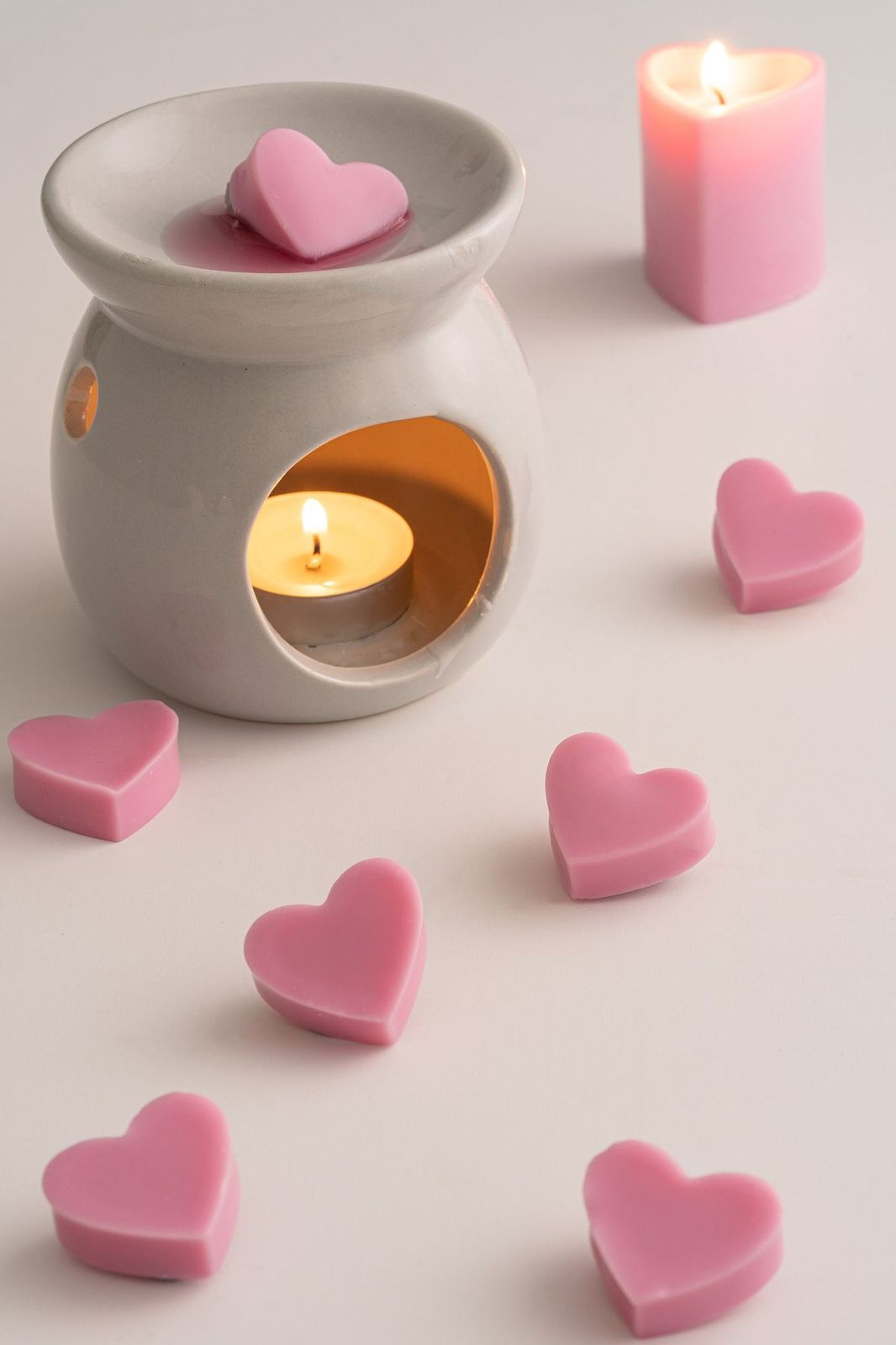 Pink heart-shaped wax melts with a white aroma burner and pink heart candle on a white background