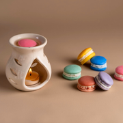 Ceramic oil burner with candle and colorful macarons on beige background