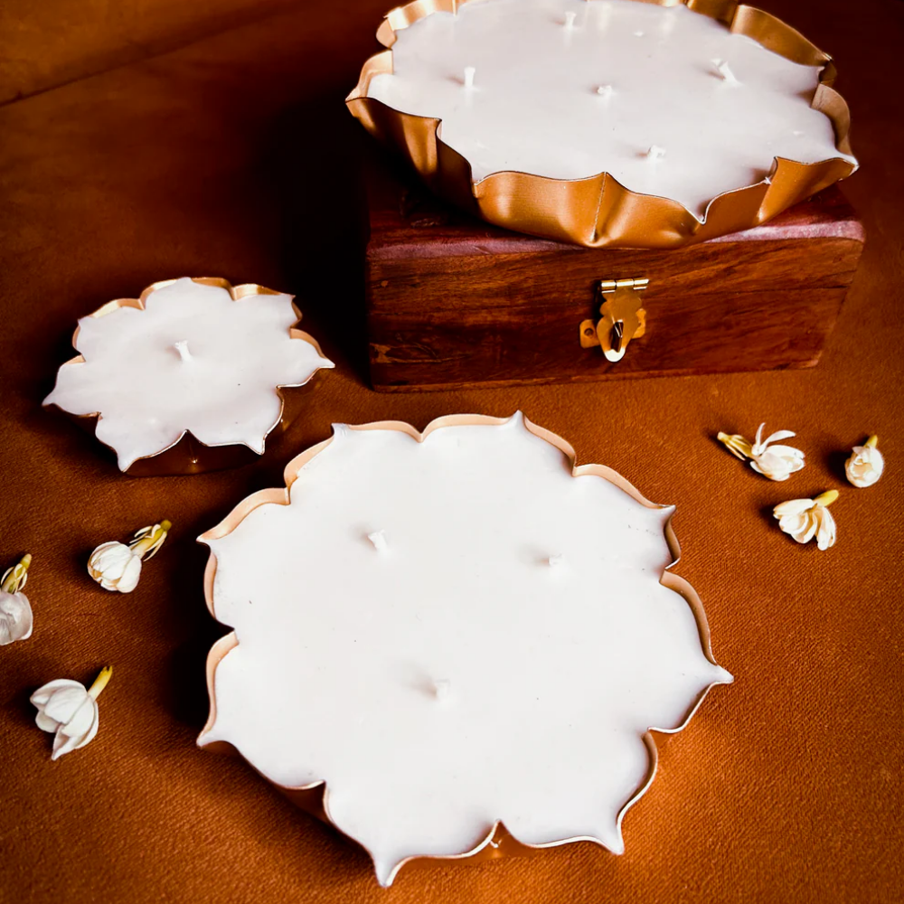 Lotus-shaped white candles in gold holders on brown surface with wooden box and white buds