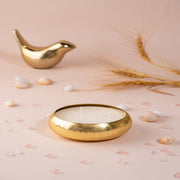 Gold bowl candle with three wicks, decorative stones, wheat, and gold bird on beige background