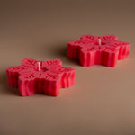 Load image into Gallery viewer, Two red snowflake-shaped candles on a plain brown background