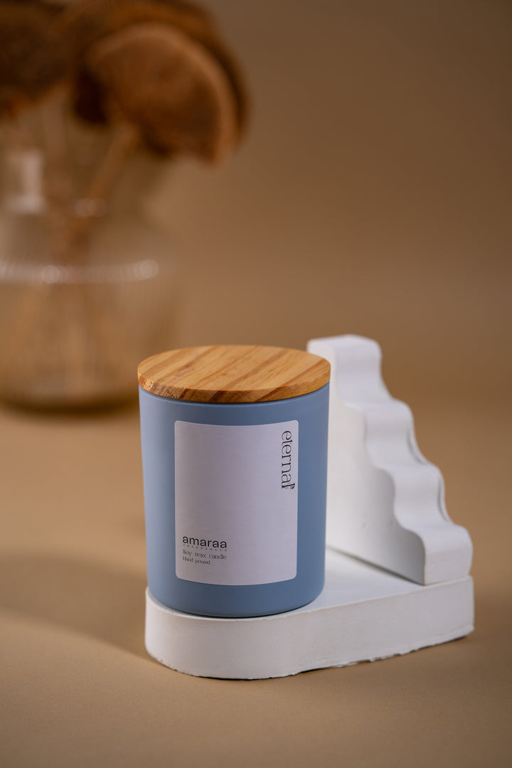 Blue Amaraa soy wax candle jar with wooden lid on white display, minimalist decor