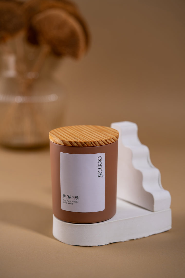 Amaraa soy wax candle with wood lid on white stand, modern beige background