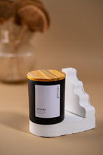 Load image into Gallery viewer, Black amaraa soy wax candle with wood lid on white stand, minimalist beige background