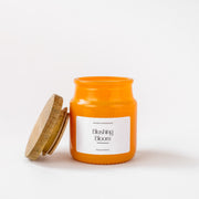 Orange glass candle jar labeled 'Blushing Bloom' by Amaraa Fragrances with wooden lid