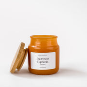 Amber glass candle jar labeled Espresso Euphoria with wooden lid on white background