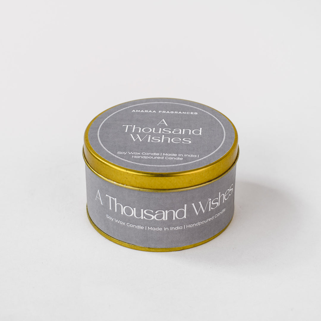 A Thousand Wishes soy wax candle in a round gold tin by Amaraa Fragrances on white background.