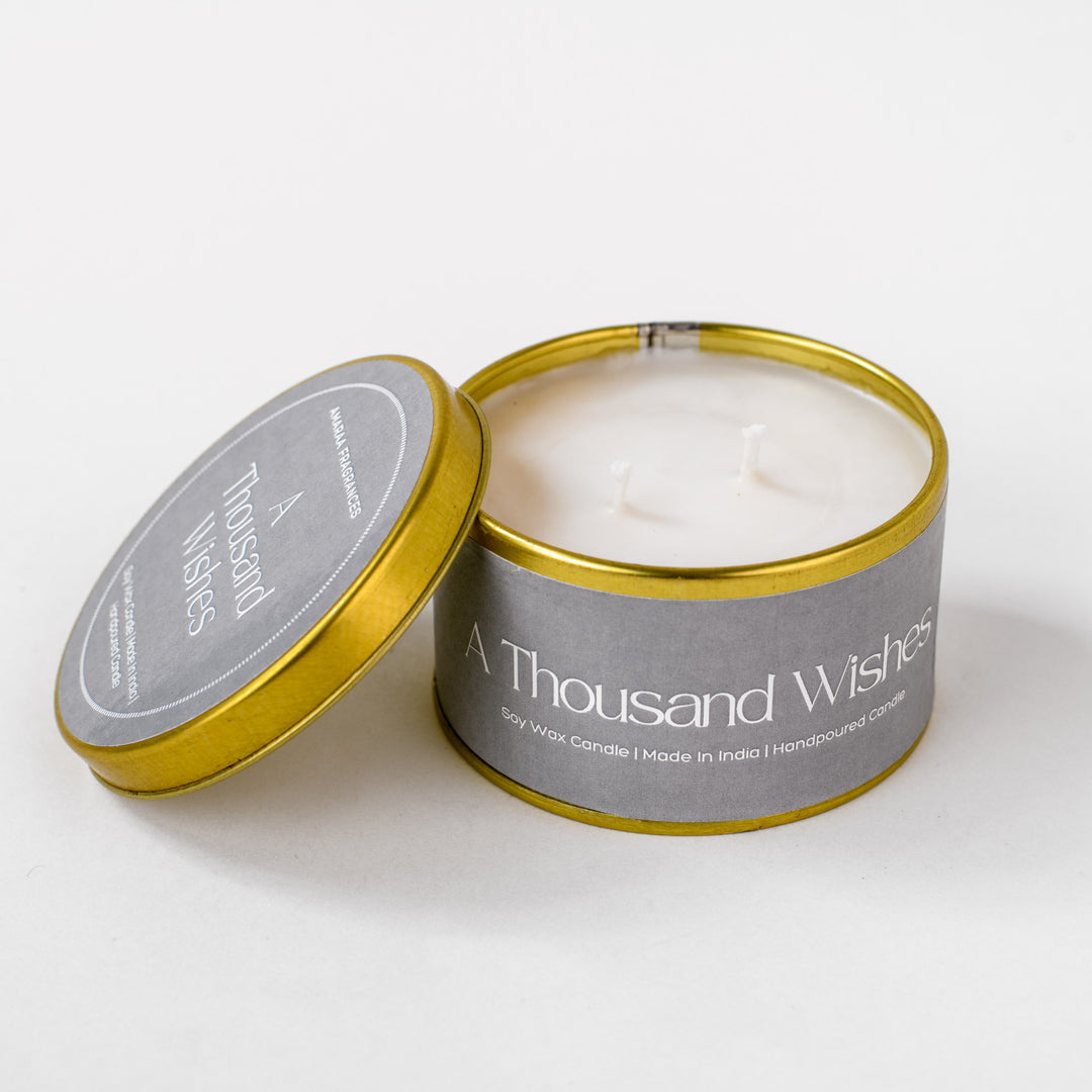 A Thousand Wishes soy wax candle in gold tin with gray label, open on white background