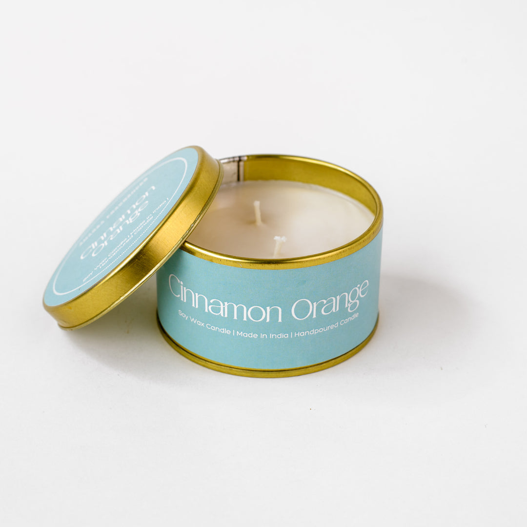 Cinnamon Orange soy wax candle in a gold tin with blue label on white background