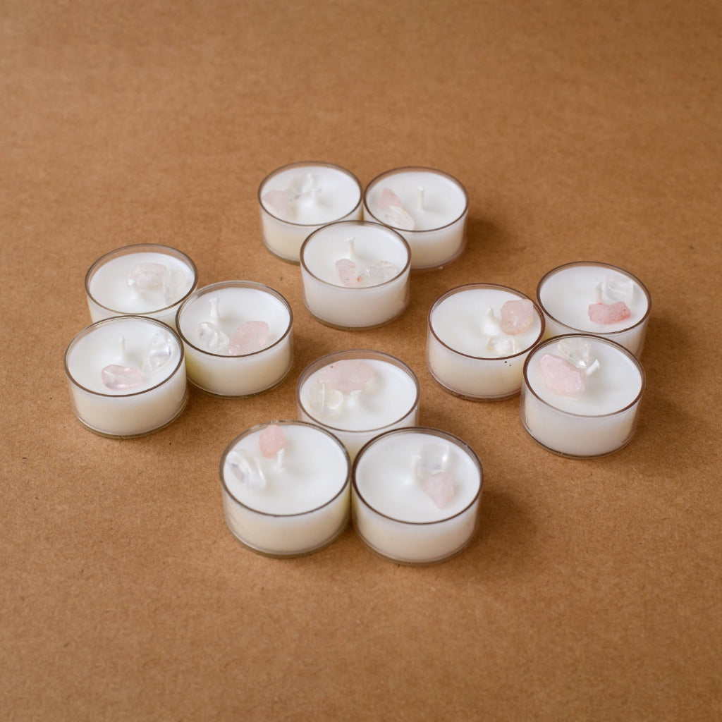 White tealight candles with quartz and rose stones on brown background