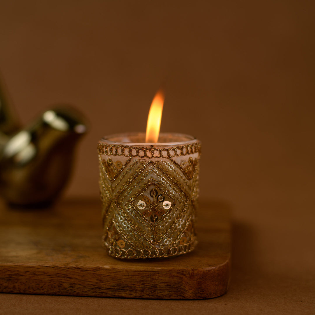 Decorative gold candle holder with lit candle on wood tray, brown background