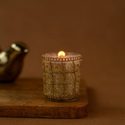 Decorative gold glass candle holder with lit candle on wooden board, brown background