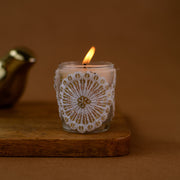 Handmade white lace-wrapped glass candle burning on wooden board, brown background
