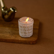 Decorative white lace candle in glass on wooden tray, brown background, cozy home decor