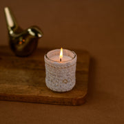 White lace-wrapped candle lit on wooden tray with gold bird decor, brown background
