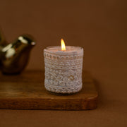 Lace-wrapped glass candle burning on wooden board with warm brown background